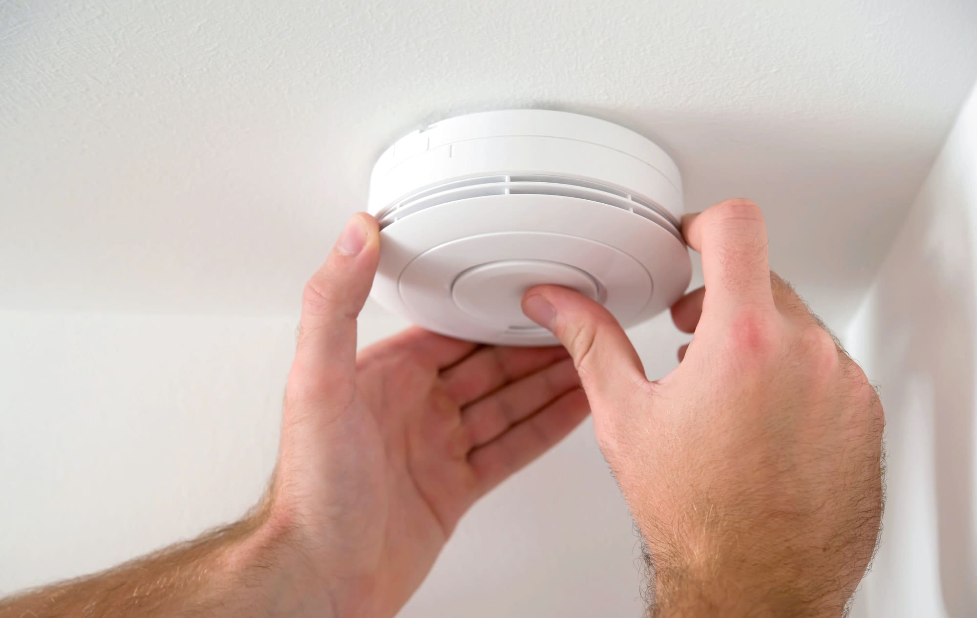 Home fire alarm inspection by technician checking detector on residential ceiling